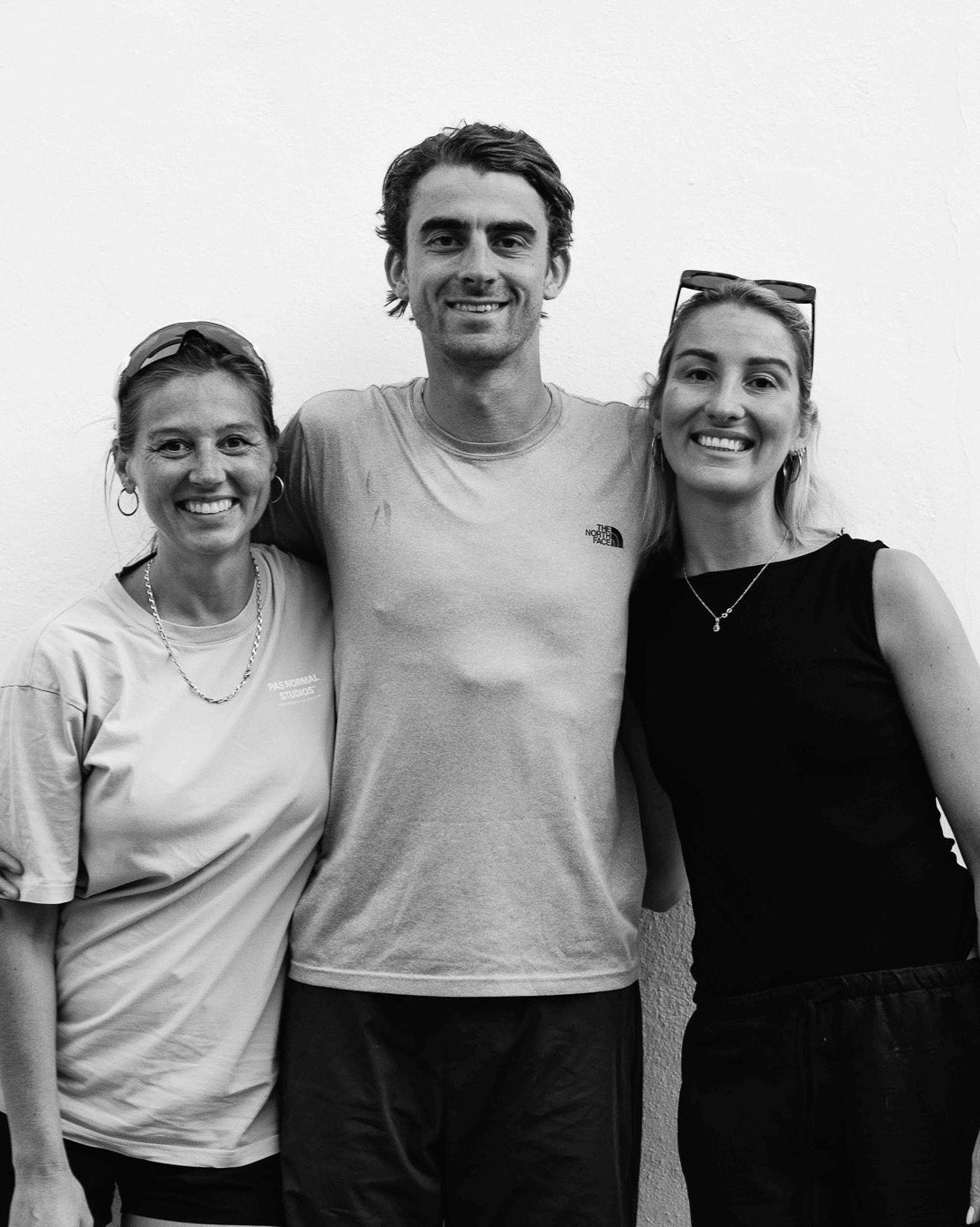 Black and white photo of three people posing together against a plain background